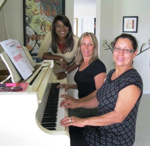 Vivia Taylor standing behind two adult students at a piano lesson