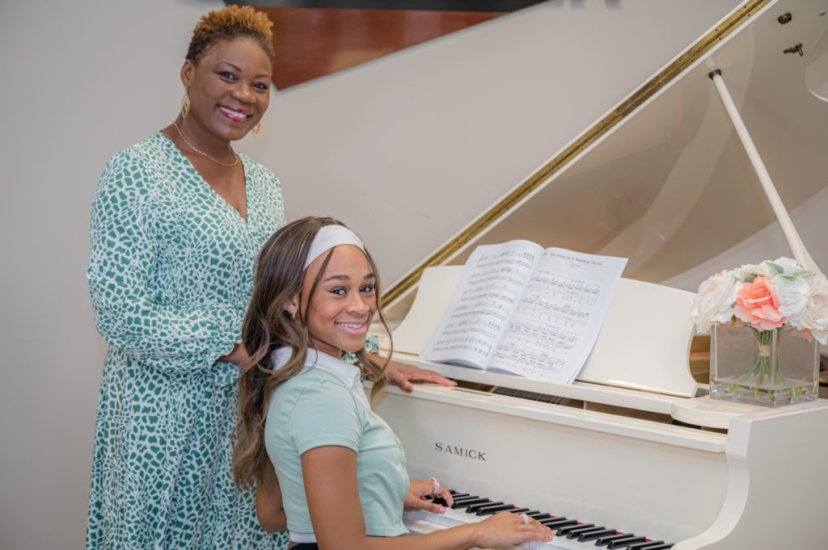 Vivia Taylor standing behind a smiling student playing piano at a performance