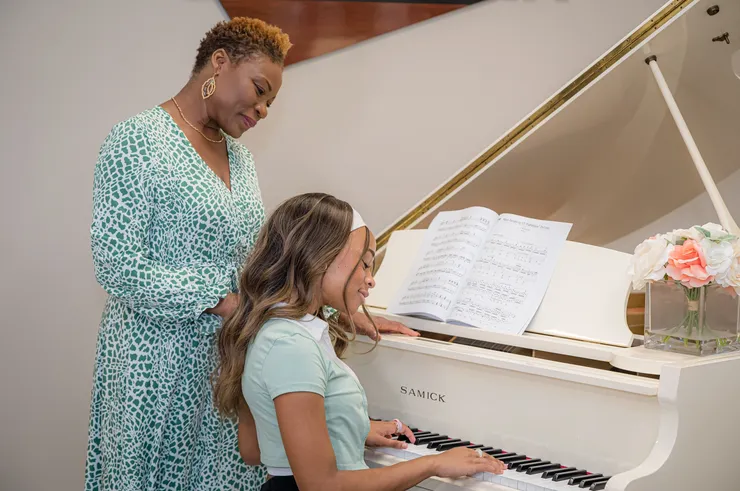 Vivia Taylor standing behind a student playing piano at a performance