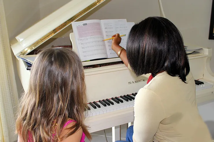 Vivia Taylor sits at a piano with a student explaining sheet music
