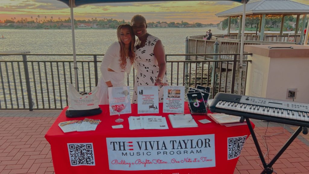 Music Teacher Vivia Taylor stands with a student behind an information table at an event.
