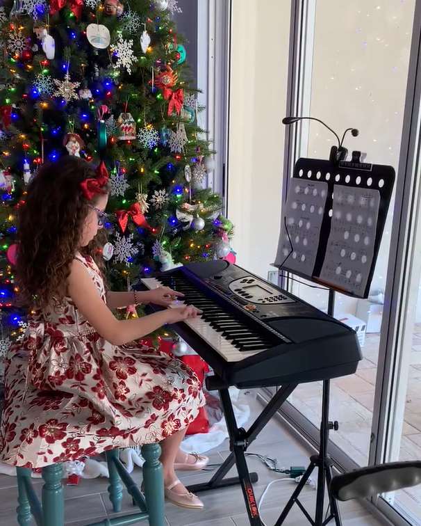 A young piano student sits at a keyboard in front of a Christmas tree.