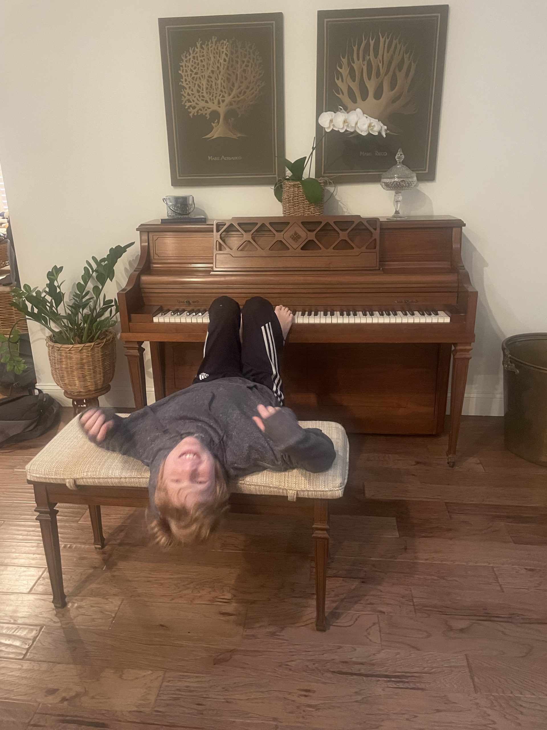 A young music student has fun at a piano, lying down on the bench and smiling.