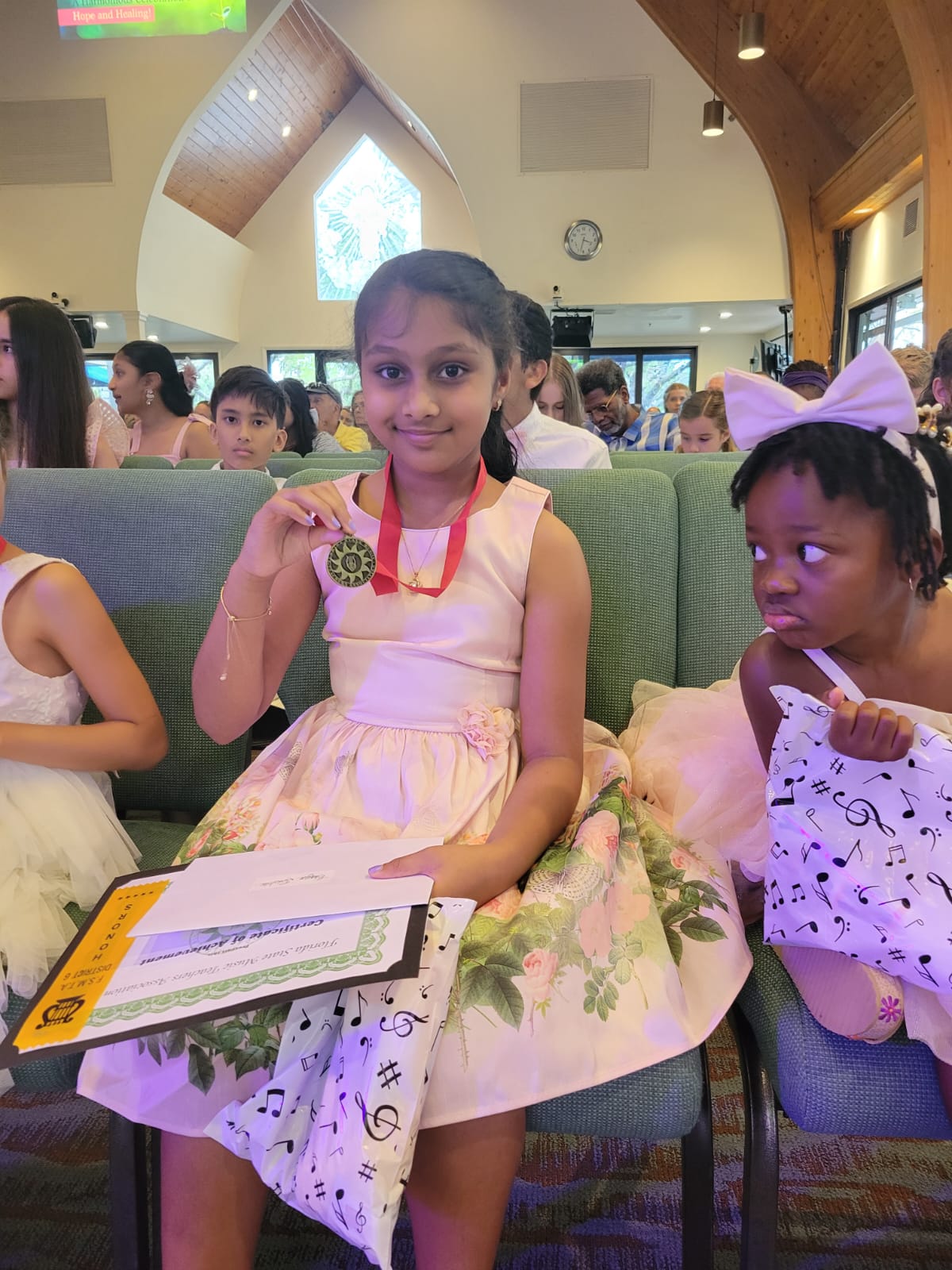 A young music student holds up a medal at a recital.
