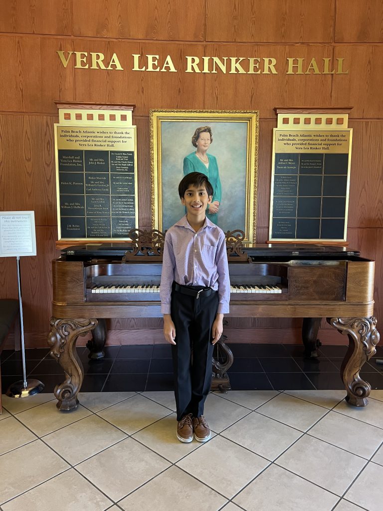 A young music student stands in front of an antique piano.