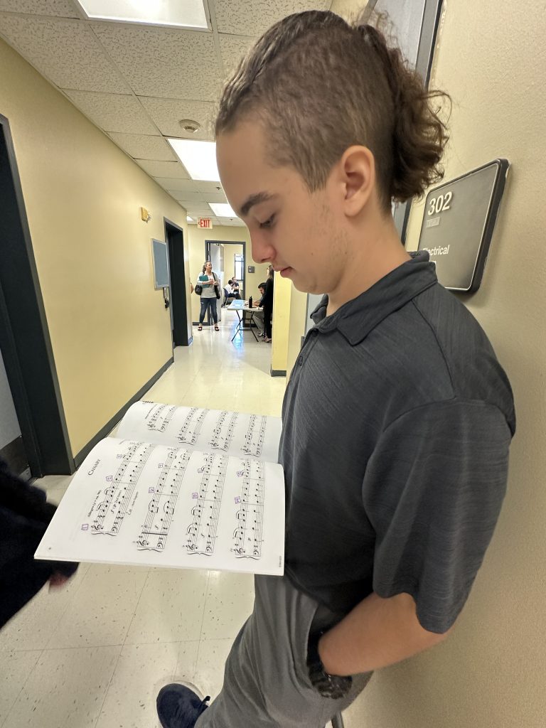 A young student waiting in a hallway before a recital reads sheet music.