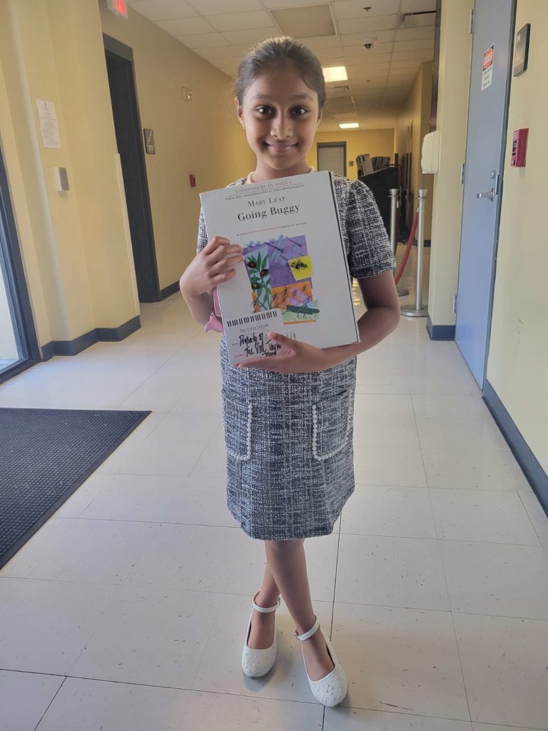 A young music student holds up a book of piano compositions.