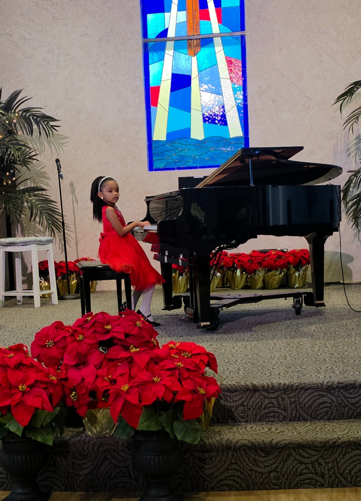 A young music student in a red dress plays piano at the 2025 Winter Recital