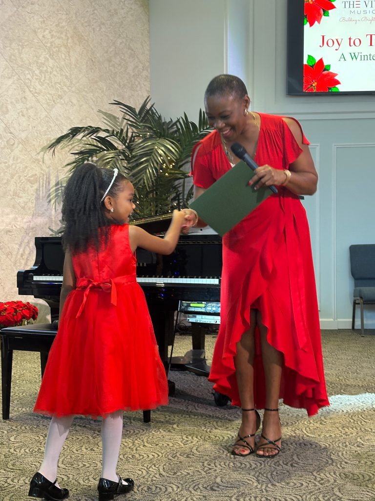 Vivia Taylor shakes a student's hand in front of a piano at the 2025 Winter Recital.