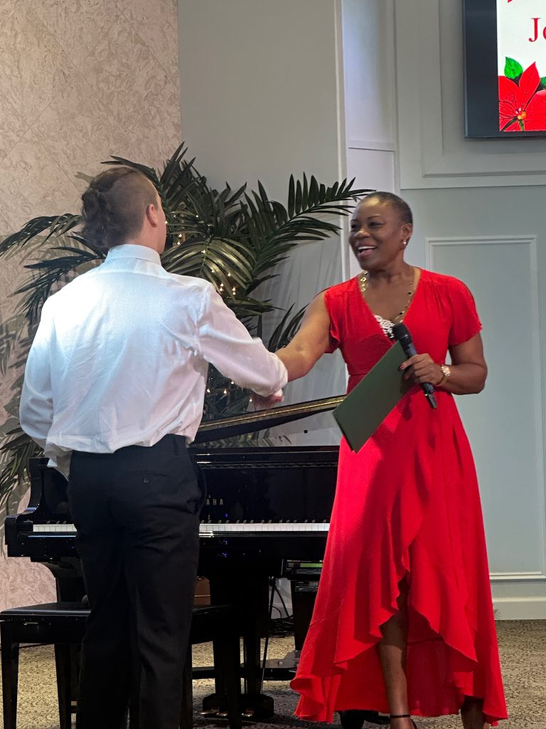 Vivia Taylor shakes a student's hand in front of a piano at the 2025 Winter Recital.